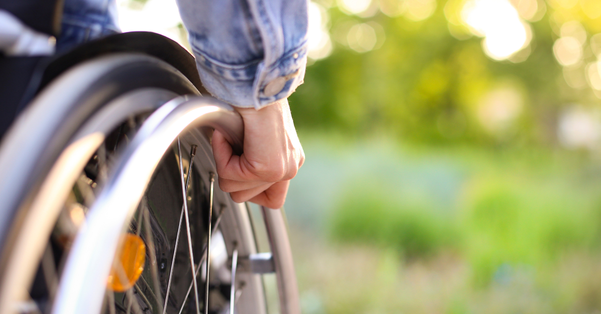 Close-up of a man in a wheel chair showing only his hand on one wheel, featured image around disability premiums