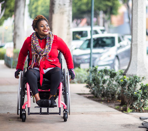 Woman on a wheelchair going down the pavement, featured image of MS life expectancy and disability