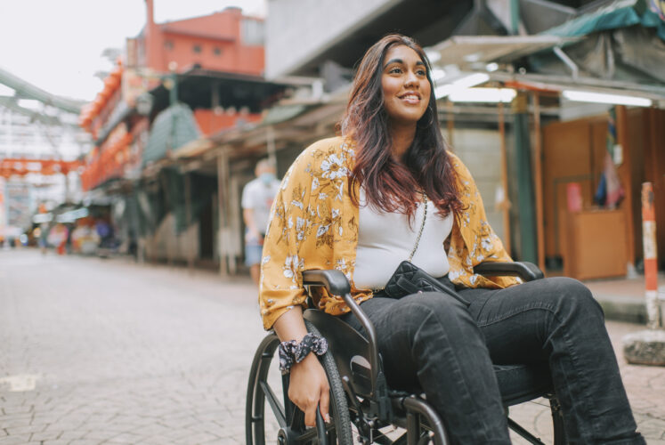 Young woman in a wheel chair going up a street - illustrating how Early disability increases risk for secondary progressive multiple sclerosis