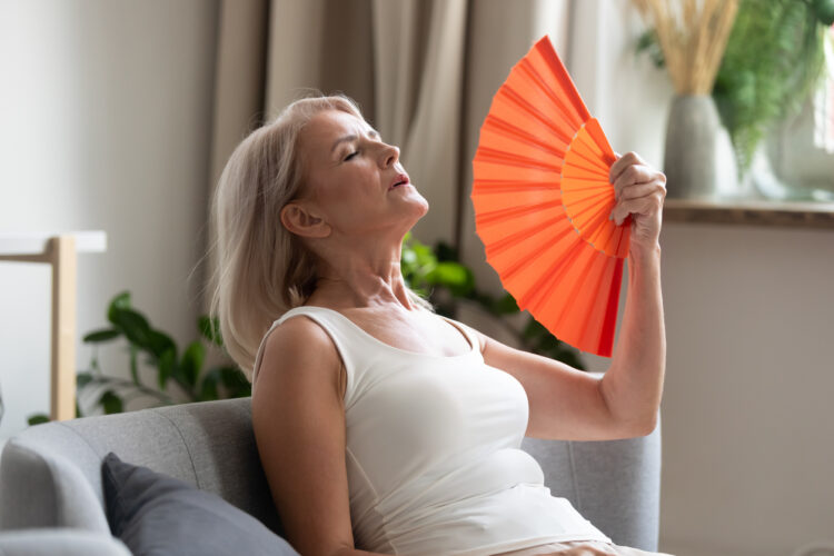 Older woman using a hand fan to illustrate hoe menopause causes reduces the number of relapses but increases disability