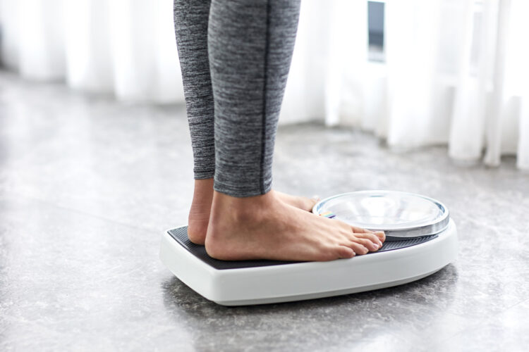 Woman on a set of scales illustrating how obesity accelerates disability and cognitive decline for MS patients