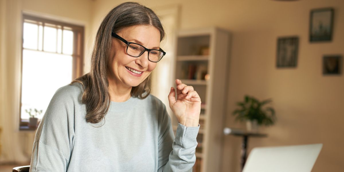 Older woman joining a Peer Pod session from her laptop in the kitchen